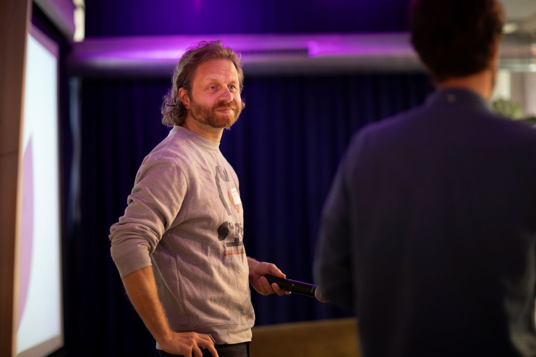 Zijaanzicht van man die voor presentatiescherm staat met een clicker in zijn hand.