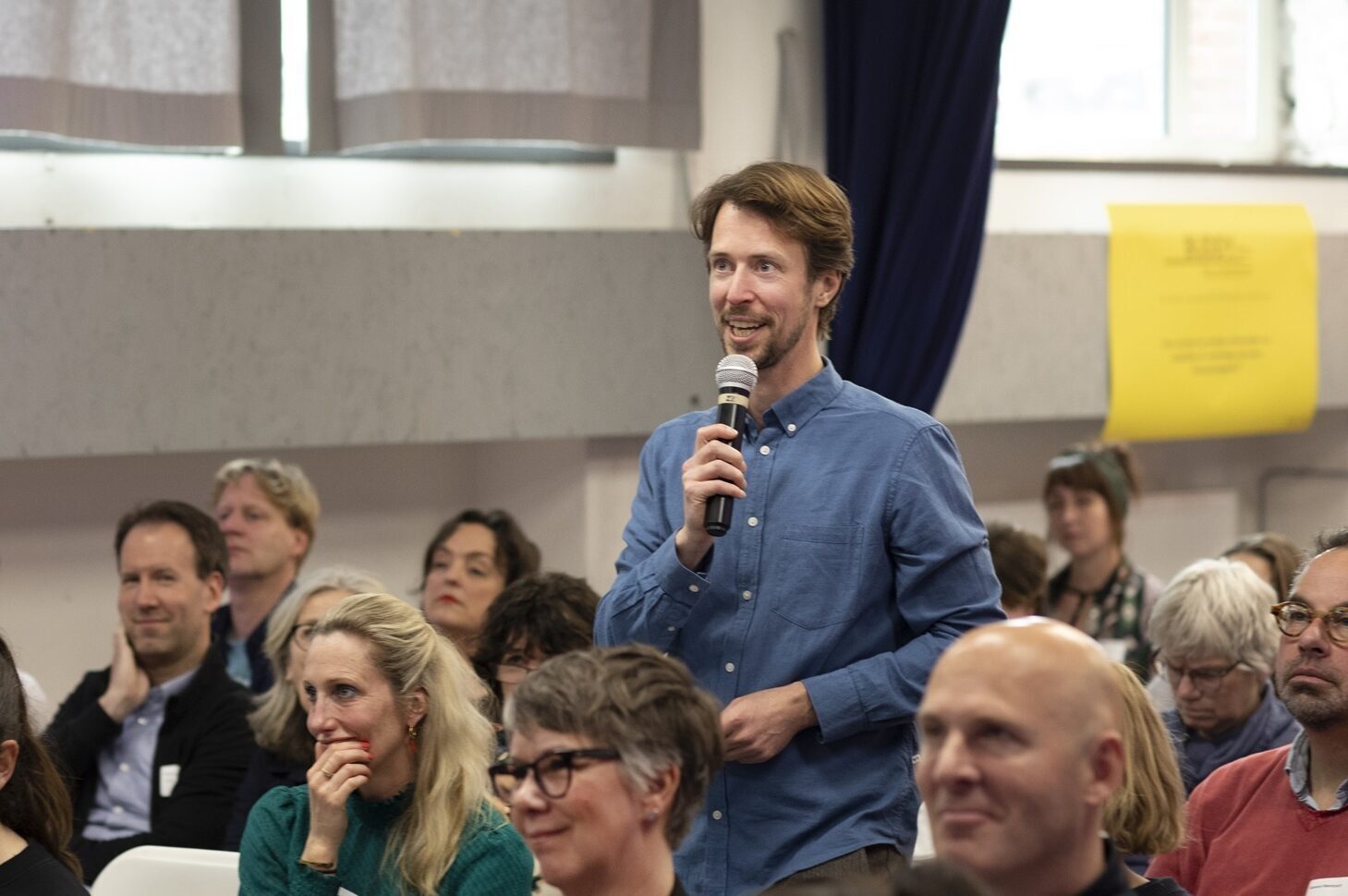 Staande man met microfoon tussen zittend publiek