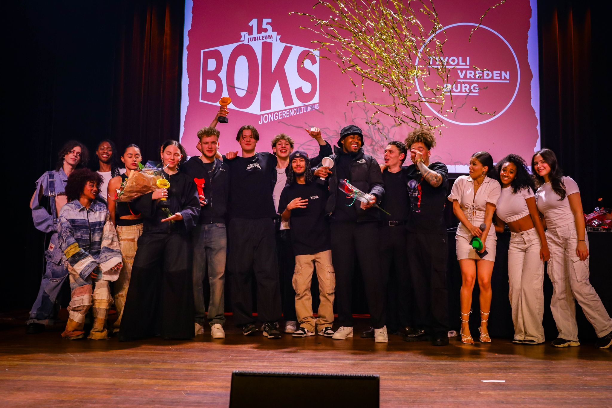 Vijftien jongeren op het podium. Enkelen houden een bokaal in handen.