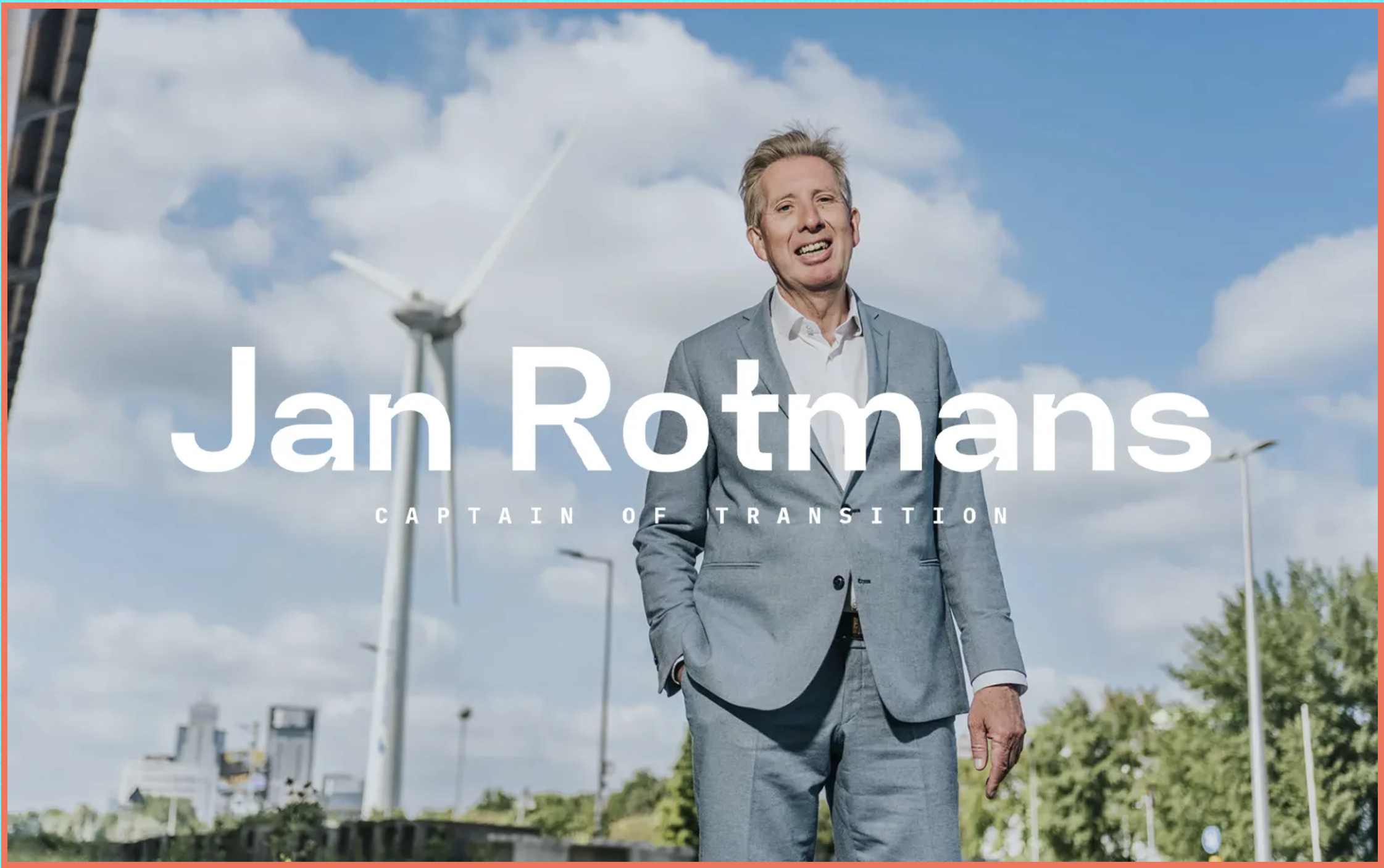 Jan Rotmans staat in een grijs pak tegen een achtergrond van een blauwe wolkenlucht en een veld vol windmolens.