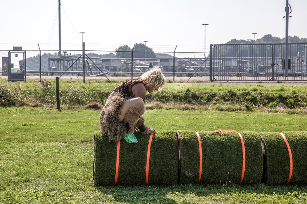 Persoon zit gehurkt op een met gras bedekte olievat met op de achtergrond een pas gesloten gaswinningslocatie