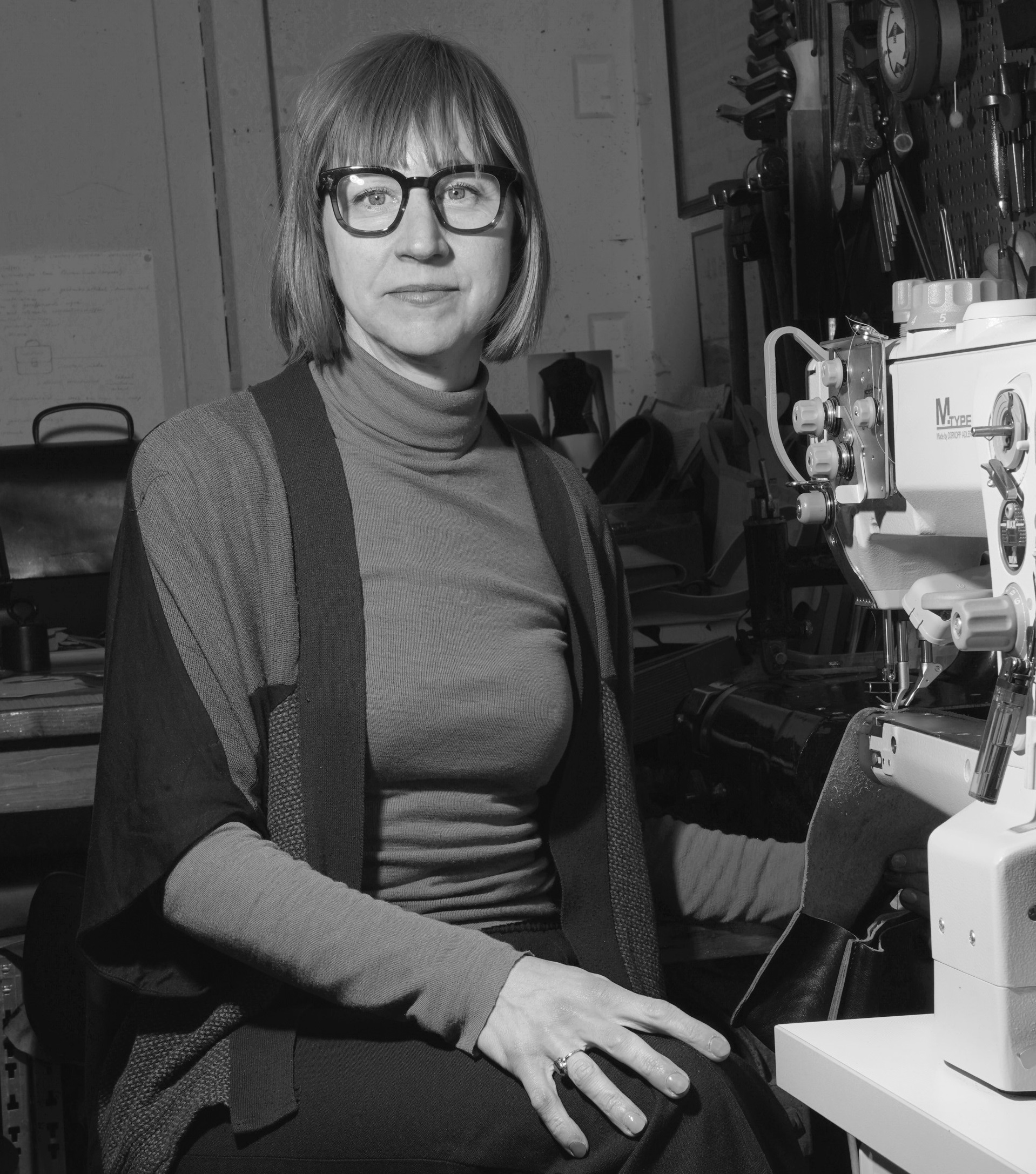 Zwart-wit foto van vrouw met bril die naast naaimachine zit.