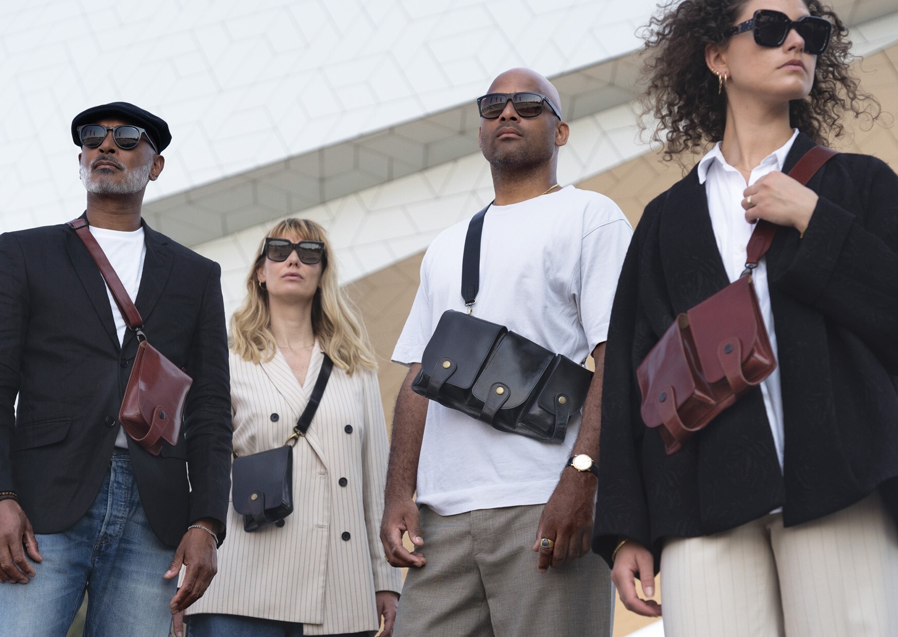 Groep van vier mensen die leren tassen (ontworpen door Noor Wentholt) om hun schouder dragen.