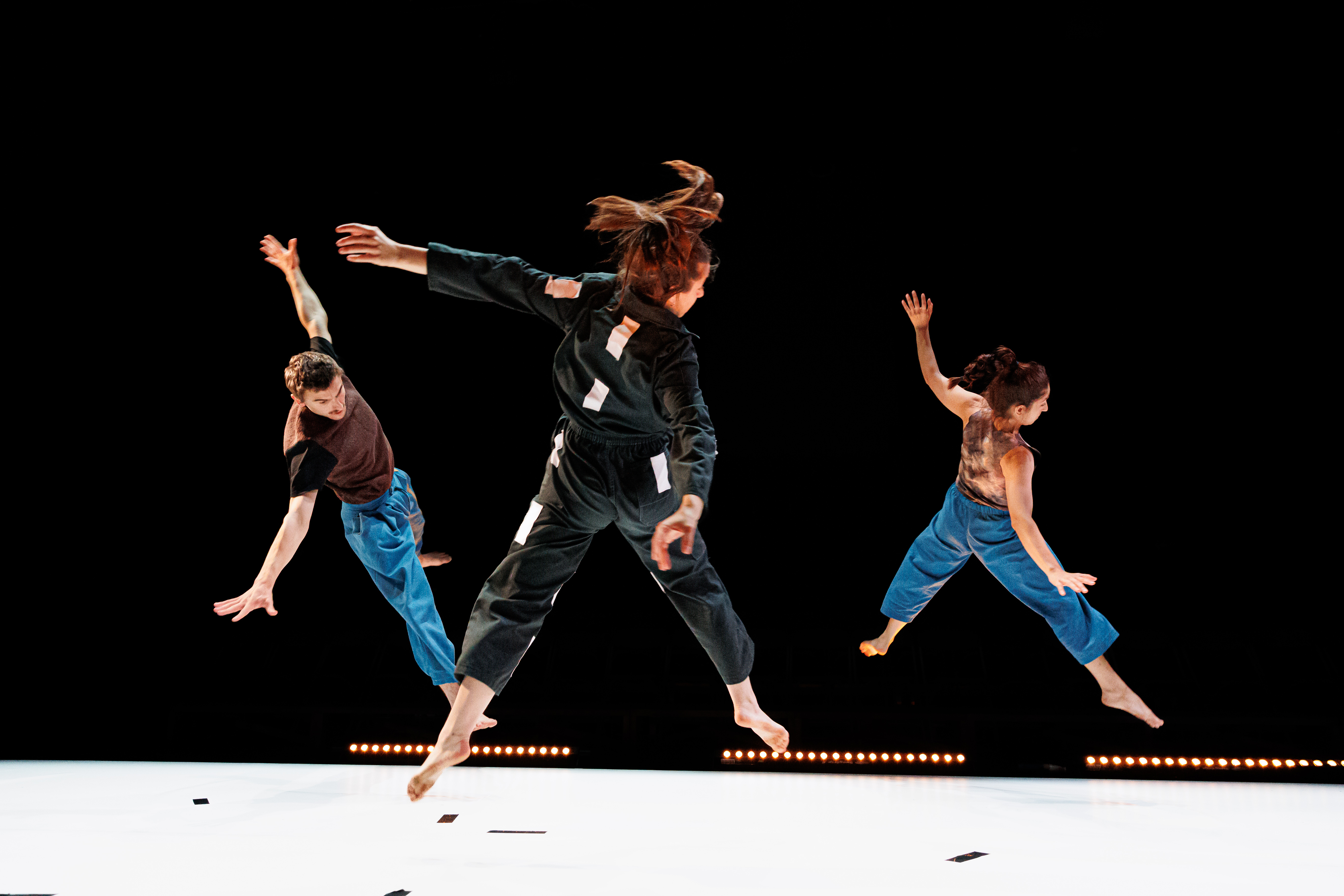 Drie personen springen met armen en benen wijd gespreid tegelijkertijd over een dansvloer.