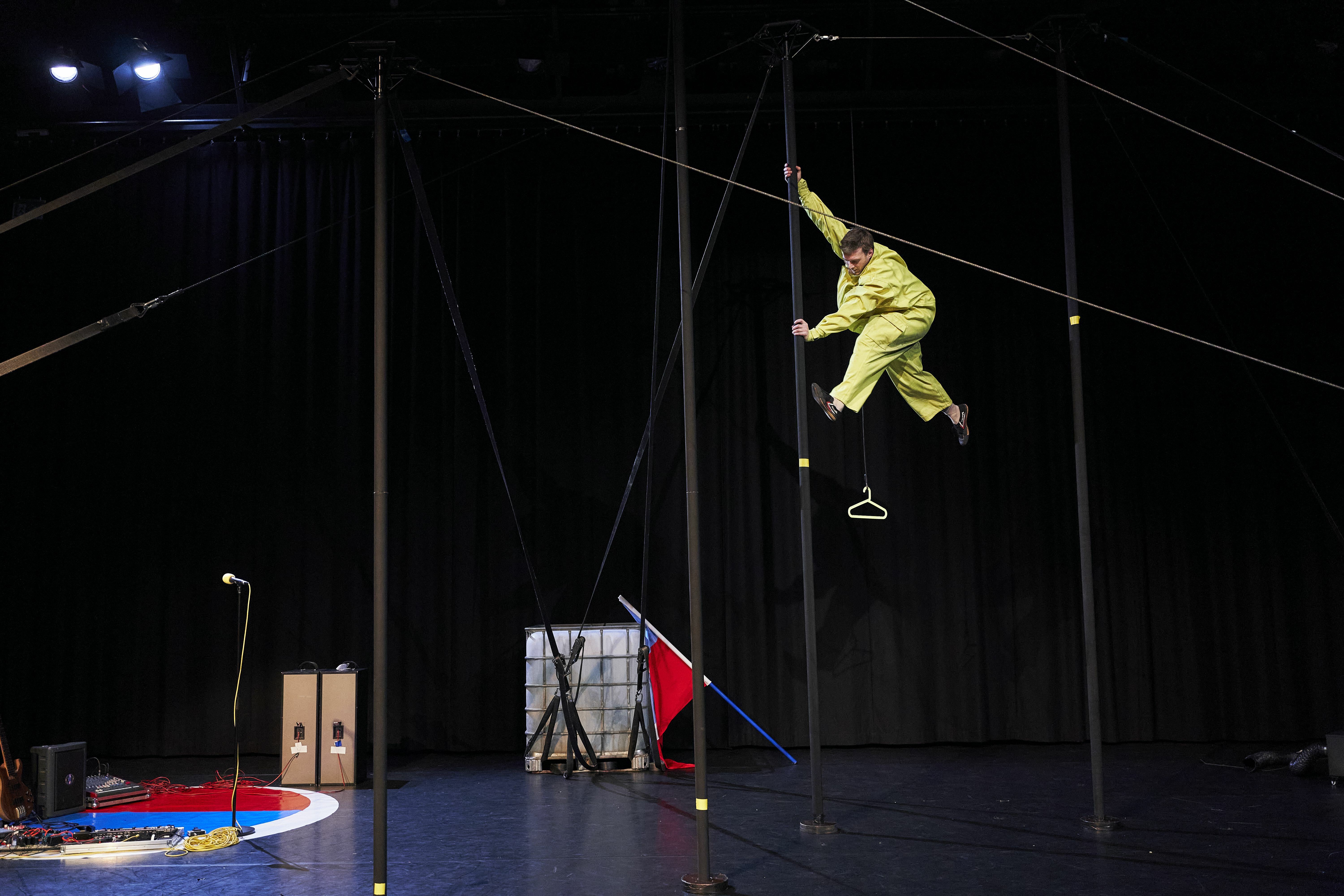 Mannelijke circusartiest in geel pak die tegen een tentpaal klimt op ongeveer 2 of 3 meter boven de grond.