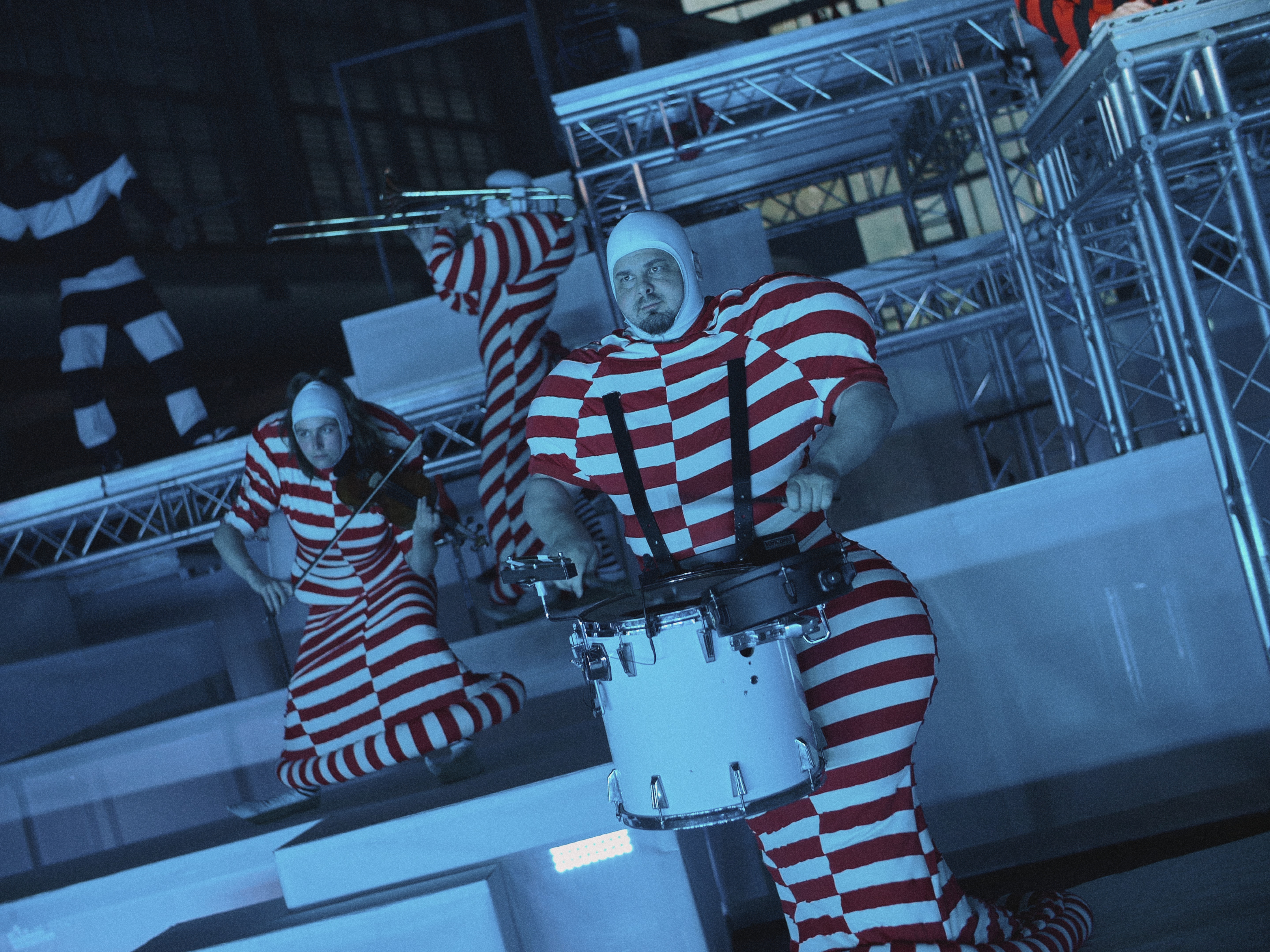 Muzikanten in rood-wit gestreepte outfits spelen op een blaasinstrument, een snaarinstrument en een percussie-instrument