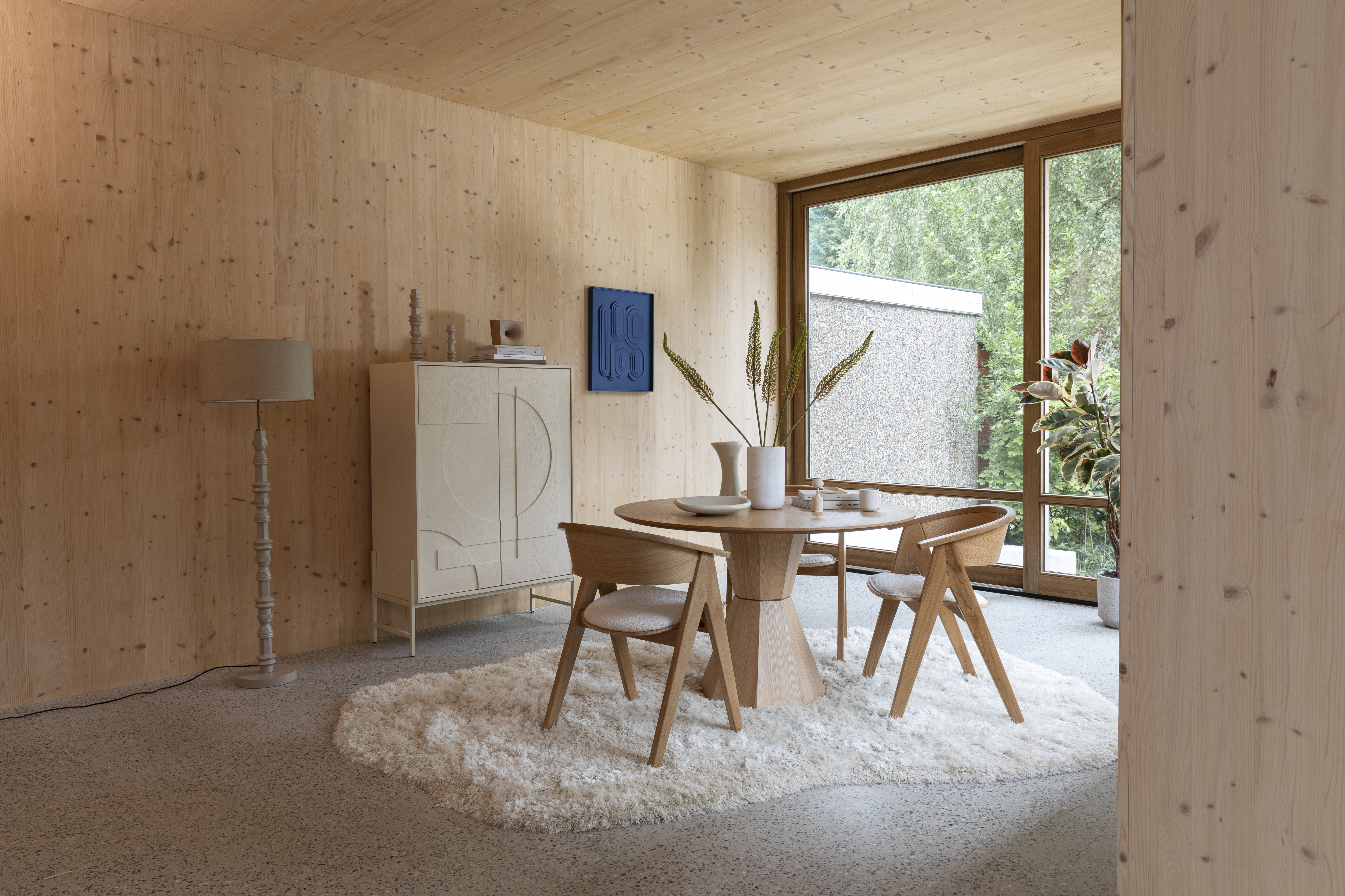Kamer met daarin een interieur van Zuiver, waaronder een houten tafel, houten stoelen, een beige vloerkleed en een staande lamp.