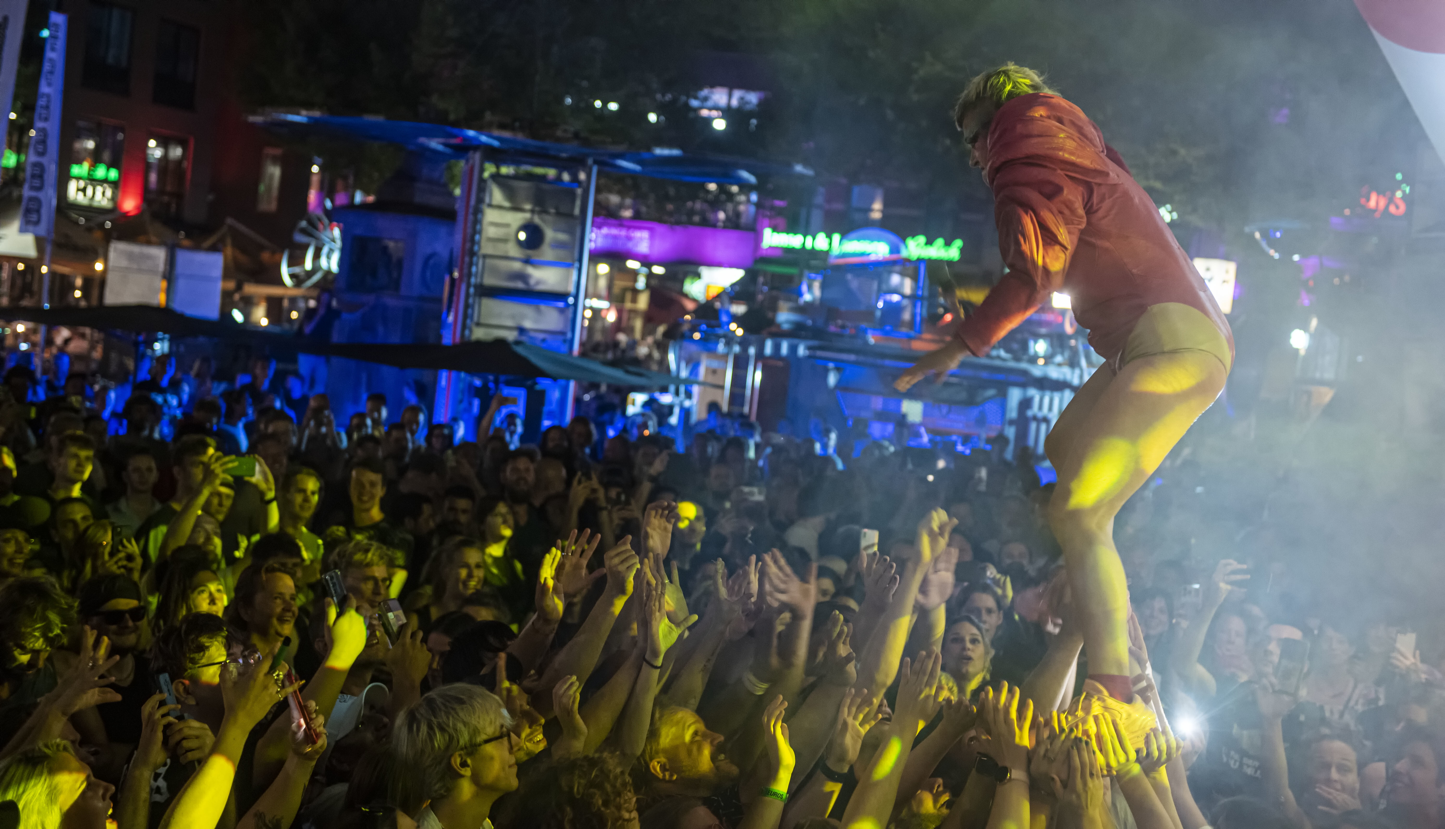 Menigte van mensen houdt de handen omhoog. Links staat artiest Peaches op de handen van enkele festivalgangers.